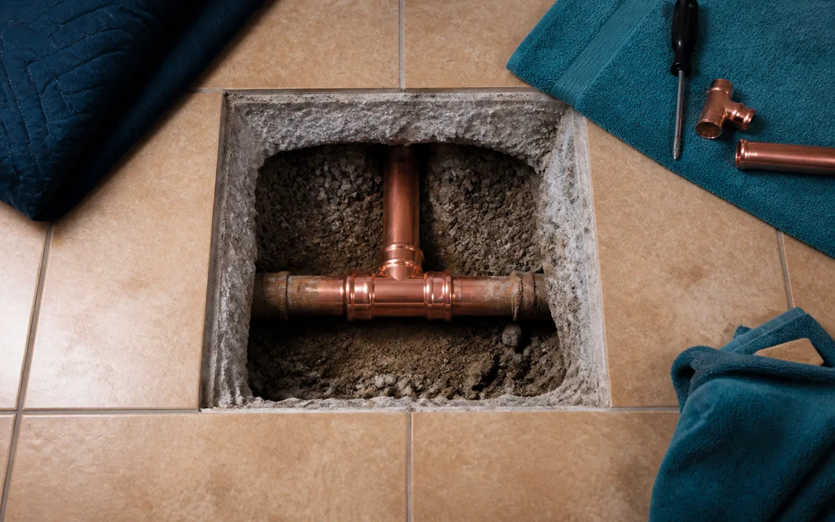 Single opened floor tile with repaired copper pipe section before re-laying